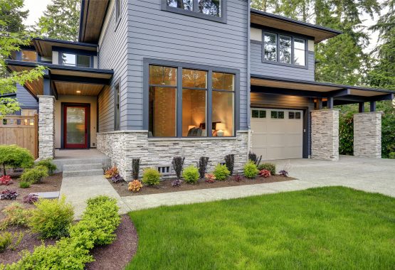 Luxurious Home Design With Modern Curb Appeal In Bellevue. Luxurious new home with curb appeal. Trendy grey two-story exterior in Bellevue with large picture windows stone foundation veneer covered porch and concrete pathway. Northwest USA